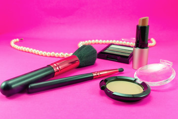 Obraz na płótnie Canvas Brushes and makeup cosmetics are placed on a pink background with pearl necklaces.