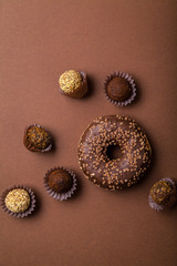 Chocolate donuts with chocolate truffles on brown background. Monochromatic concept.