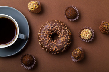 Chocolate donuts with truffles and cup of black coffee on brown background. Monochromatic concept.