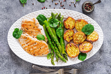 Chicken fillet cooked on a grill with a garnish of asparagus and baked potatoes. Dietary menu. Healthy food. Flat lay. Top view