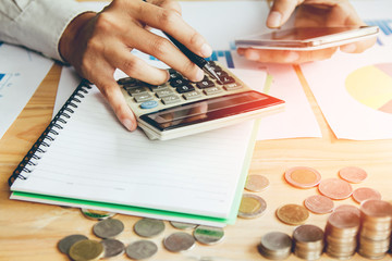 Business man or accountant in gray shirt holding pen working on accounts and using  calculator and writing on desk, With sunset light.