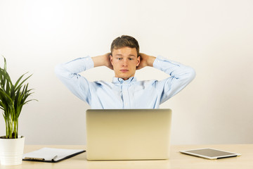 Male office worker looking on laptop computer with arms up, relaxed pose in work day.