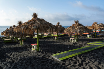 Tanning beds and straw umbrellas on Perissa beach, Santorini island, Greece.
