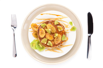 Stack of pancakes isolated on white background. Delicious breakfast with a grilled bananas and a caramel, kiwi slices. Top view, flat lay