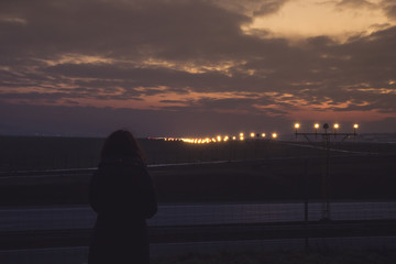 A young girl looks on the runways at the airport with landing lights illuminated at sunset © Bogdan