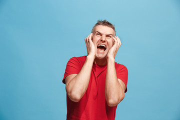 The young emotional angry man screaming on blue studio background