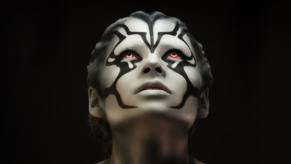 Watchfully looking and  intently looking after.Creative appearance of alien creature with red  eyes and black and white skin is created through a make-up and body-art