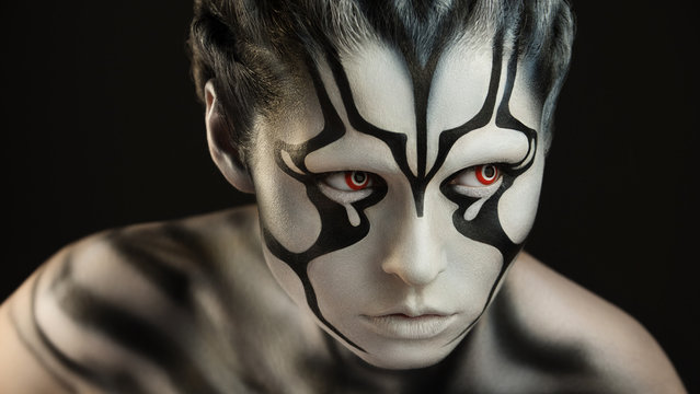 Intently and watchfully  looking alien creature with the brightly expressed red lenses and skin of black and white color created through a make-up