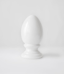 Single white decorative ceramic statuette egg in egg-cup on white table top background. Easter religious Christian symbol.