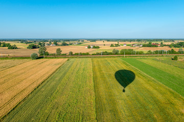 Cień balonu lecącego nad polami z widokiem na horyzont.