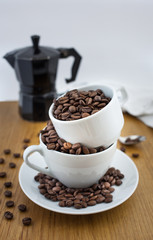 Coffee beans in the cup and coffee percolator on wooden table with white background