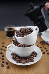 Espresso shot, coffee beans in the cup and coffee percolator on wooden table with black background
