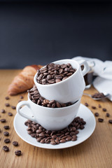 Espresso shot, coffee beans in the cup and croissant on wooden table with black background