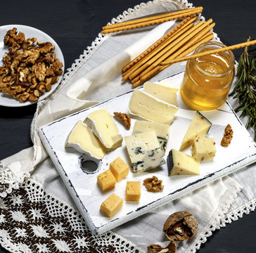 pieces of different cheese on a white wooden board near a jar with honey