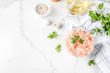 Raw chicken or turkey minced meat in white bowl,  with oil, spices and herbs on light background. Copy space top view