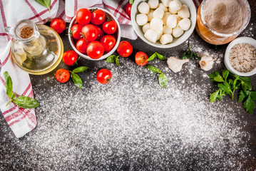 Homemade pasta pizza italian food ingredient on dark rusty table with flour, olive oil, basil, tomatoes and kitchen accessories top view