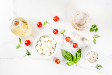 Homemade pasta pizza italian food ingredient on white marble table with flour, olive oil, basil, tomatoes and kitchen accessories top view