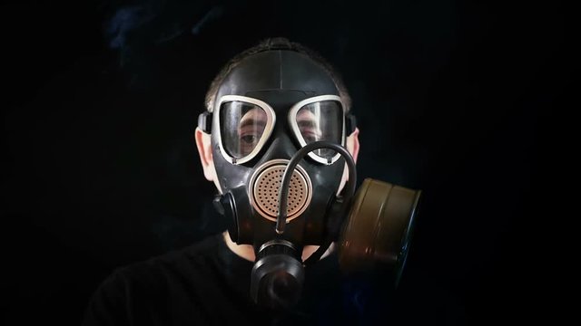 Face of a man in a gas mask on a black background. Smoke around a person