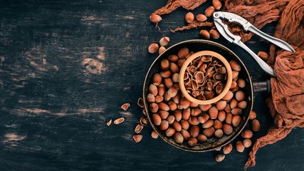 Hazelnut in a frying pan. On a black wooden background. Top view. Copy space for your text.