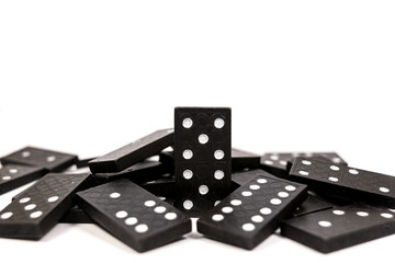 One black wooden domino chain standing before fallen dominoes on a white background. Logical Game. Business concept. Space for text.