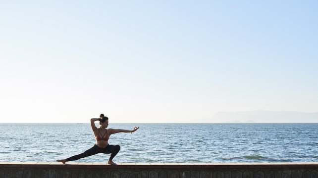Young woman practicing yoga on a wall by the sea