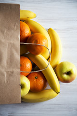 Paper bag of different fruits on white wooden background. Flat lay. Top view.