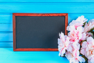 Pink peonies with a chalkboard on a blue wooden table. Postcard for the holiday. Copy the space.