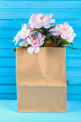 Pink peonies in a craft pack on a blue wooden table. Postcard for the holiday.