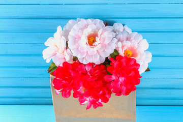 Pink peonies in a craft pack on a blue wooden table. Postcard for the holiday.