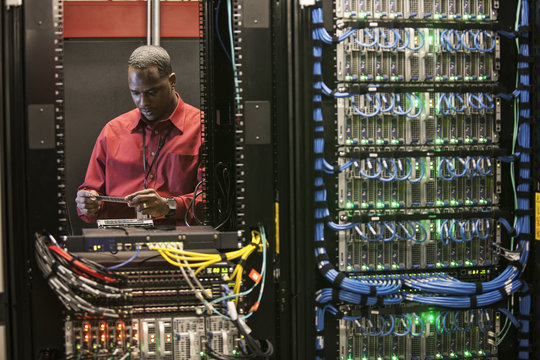 Black man technician working on computer servers in server farm.