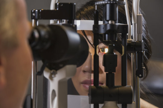 Caucasian man ophthalmologist using a slit lamp tonometer on a patient's eye.