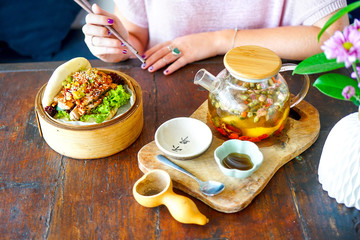 Grilled tuna and guacamole bao. Female hand with chopsticks. Wooden table background in a restaurant. Teapot of green Chinese tea. Traditional Chinese and French cuisine. Top view with copy space