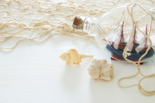 nautical concept image with white fishnet, seashells and sail boat in the bottle over white wooden table.