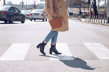 street style portrait of an attractive woman wearing a beige trench coat, denim jeans, ankle boots, cat eye sunglasses and a metallic handle brown tote bag. fashion outfit perfect for sunny spring day