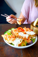 Salad with smoked salmon in slices of soft bread with a delicate cream. Restaurant with a wooden table. A girl in pink sits at a table and eats a salad. Side view with copy space and close-up
