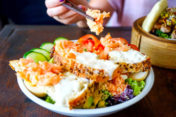 Salad with smoked salmon in slices of soft bread with a delicate cream. Restaurant with a wooden table. A girl in pink sits at a table and eats a salad. Side view with copy space and close-up