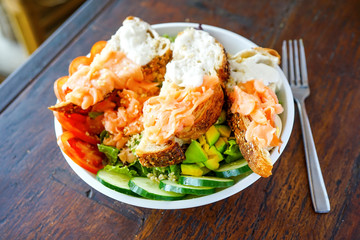 Salad with smoked salmon in slices of soft bread with a delicate cream. Restaurant with a wooden table. A girl in pink sits at a table and eats a salad. Top view with copy space