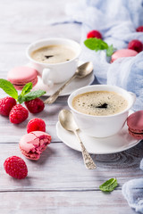 Cup of coffee with french raspberry macaroons cookies on vintage white background. Holidays food concept.
