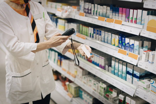 Midsection of female owner using bar code reader on medicine standing by rack at store