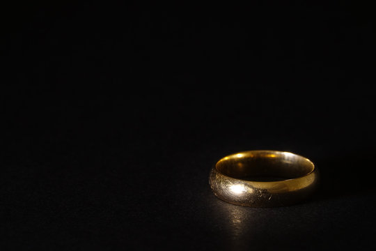 A scratched used old gold wedding ring on black background. Copyspace for text.