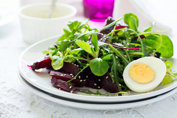 Fresh salad with beetroot, mix leaves, olive oil, egg and sesame seeds on white table cloth