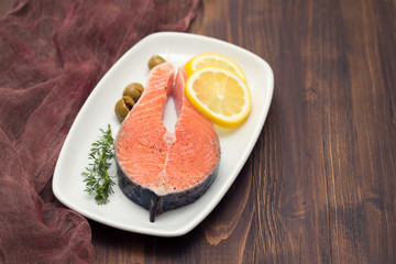 raw salmon with lemon on white dish on brown background