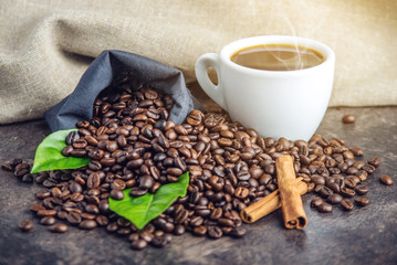 White black espresso Cup with a pile of coffee beans and green leaves in bag on white linen background