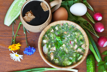 Summer cold soup Okroshka with fresh greens and sour cream and a mug of bread kvass on a wooden table. Traditional Russian cuisine. Rustic Still Life