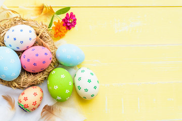 Obraz na płótnie Canvas Happy easter! Colorful of Easter eggs in nest with red ribbon, Feather and paper star on pastel color bright yellow and white wooden background.