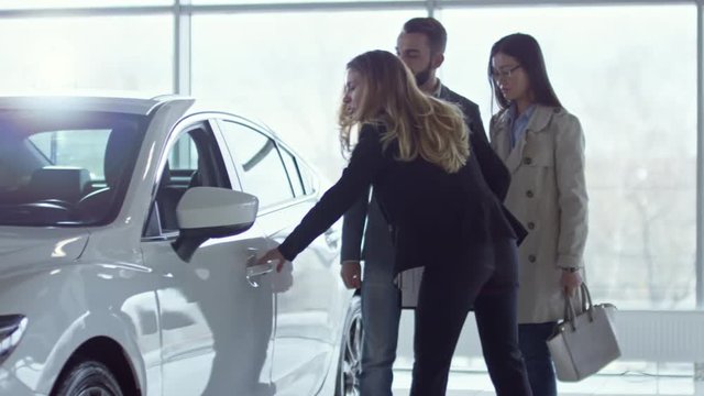 Medium shot of professional saleswoman in formalwear showing new car to young couple at dealership