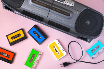 Old black retro cassette music audio tape recorder and retro cassette tape collection on pink background