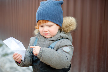 The boy is upset, holds a paper boat in his hands