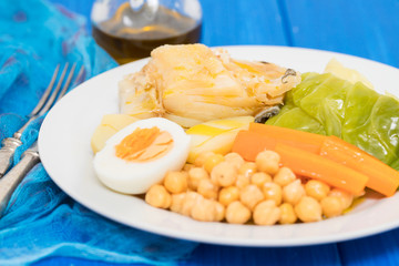 boiled cod fish with potato, carrot, cabbage , chick-pea and egg on white plate