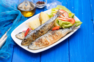 grilled sardines with boiled potato and salad on white plate